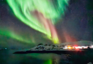 L'aurora boreale sopra un'isola innevata e una baita illuminata a Engvik Hytta 83699, in Svezia.