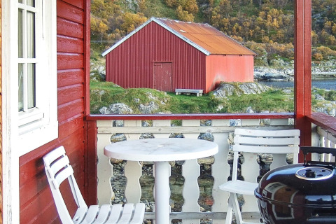 Vista dal portico di una baita rossa con sedie bianche, tavolo e barbecue verso un fienile rosso in Svezia.
