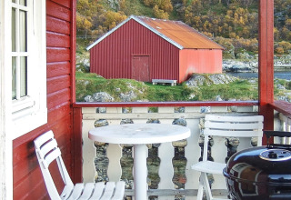 Vista dal portico di una baita rossa con sedie bianche, tavolo e barbecue verso un fienile rosso in Svezia.