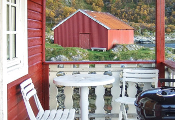 Vista desde el porche de una cabaña roja con sillas blancas, mesa, barbacoa y un granero rojo en Suecia.