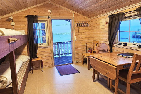 Interno di cabina in legno con letto a castello, tavolo da pranzo e vista lago a Engvik Hytta, Svezia.