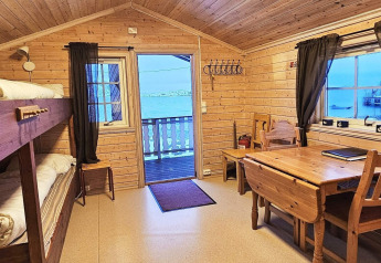 Interior de cabaña de madera con literas, mesa de comedor y vista al lago en Engvik Hytta, Suecia.