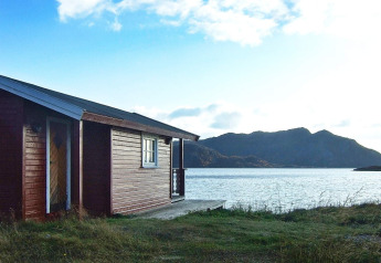Cabaña roja de madera junto al agua, con montañas al fondo, tomada en Engvik Hytta 83699 en Suecia.