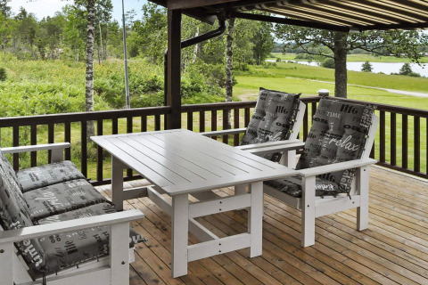 Veranda con mobili da esterno bianchi e cuscini su pavimento in legno, vista natura a Frändefors, Svezia.