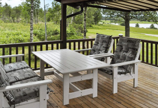 Terraza con muebles de exterior blancos y cojines sobre tarima de madera, vista a la naturaleza en Frändefors, Suecia.