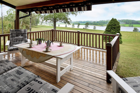 Terrazza in legno di una casa vacanze a Frändefors, Svezia, con vista su lago e prati verdi.