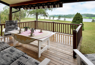 Terraza de madera en casa de vacaciones en Frändefors, Suecia, con vistas a lago y prados verdes.