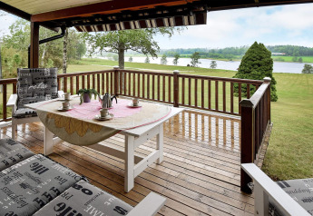 Terraza de madera en casa de vacaciones en Frändefors, Suecia, con vistas a lago y prados verdes.