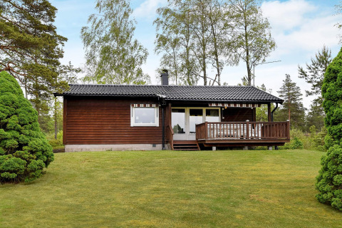 4-persoons vakantiehuis in Frändefors met houten gevel, veranda, groen gras en bomen op de achtergrond.