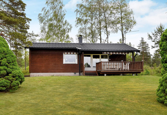 Casa de vacaciones para 4 personas en Frändefors con fachada de madera, césped y árboles alrededor.
