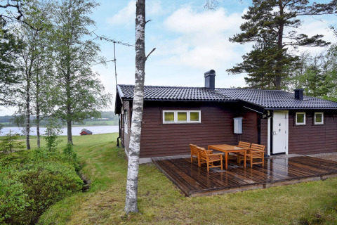 Chalet au bord du lac à Frändefors, Suède, avec terrasse en bois et salon de jardin entouré d’arbres.