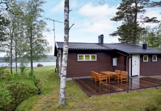 Chalet au bord du lac à Frändefors, Suède, avec terrasse en bois et salon de jardin entouré d’arbres.