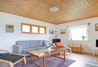 Wohnzimmer mit Holzdecke, modernen Möbeln und großen Fenstern in einer 4-Personen-Hütte in Frändefors, Schweden.
