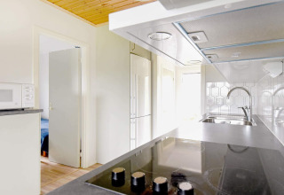 Moderne Küche in einer Ferienhütte in Frändefors, Schweden, mit Kochfeld, Spüle und Tür zum Schlafzimmer.