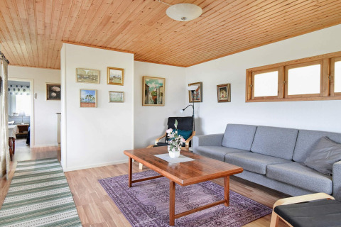 Wohnzimmer eines Ferienhauses in Frändefors, Schweden, mit Holzdecke, grauem Sofa und Wandbildern.