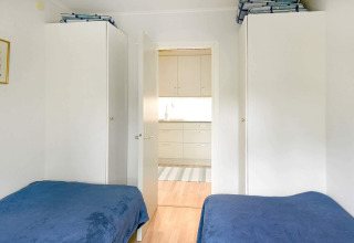 Slaapkamer met twee eenpersoonsbedden, witte kasten en open deur naar keuken in Zweedse vakantiewoning.