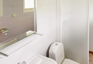 Helles Badezimmer in einem Ferienhaus in Frändefors, Schweden, mit Toilette, Spiegel und Glasablage.