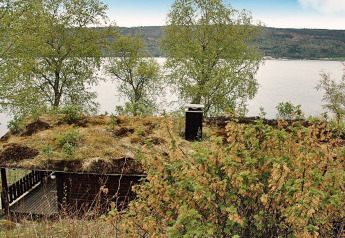 Chalet avec toiture herbeuse au bord d’un lac en Suède, entouré d’arbres et vue sur l’eau.