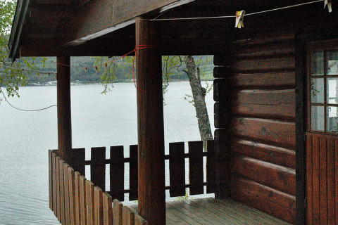 Holzveranda an einem Ferienhaus am See in Schweden, mit Blick auf das Wasser und bewaldete Hügel.