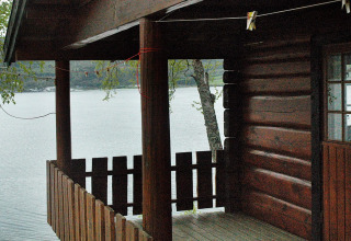 Houten terras van een chalet aan het meer in Zweden, met zicht op het water en bosrijke heuvels.