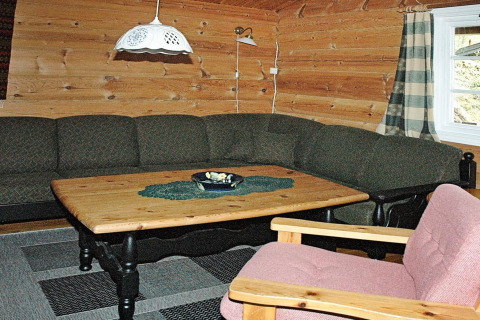 Wood-paneled living room with green corner sofa, wooden table and pink chair in 4 person holiday home in Surna, Sweden.