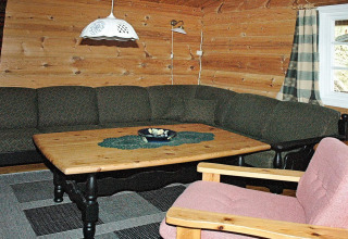 Woonkamer met houten wanden, groene hoekzetel, houten tafel en roze stoel in 4-persoons vakantiehuis in Surna, Zweden.