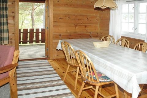 Lichte houten eetkamer met zes stoelen, een tafellaken en terraszicht in chalet Surna, Zweden.