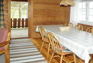Lichte houten eetkamer met zes stoelen, een tafellaken en terraszicht in chalet Surna, Zweden.