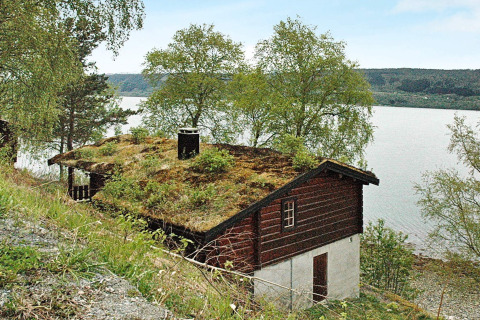 Traditioneel Zweeds chalet met grasdak aan een meer, omgeven door bomen en uitzicht op water.