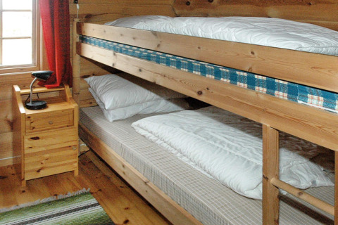 Interior de cabaña de madera con literas, mesita de noche y lámpara en casa vacacional en Surna, Suecia.