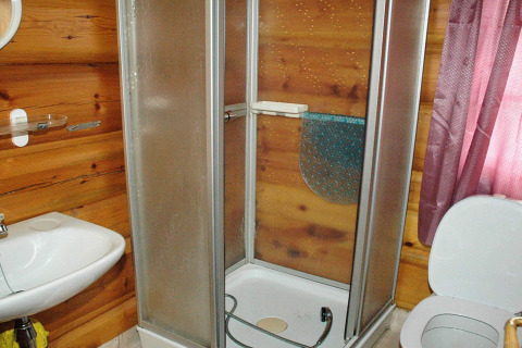 Badeværelse i træchalet med brusekabine, håndvask, toilet og pink gardin i Surna, Sverige.