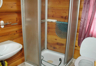 Bagno in chalet di legno con box doccia, lavandino, WC e tenda rosa a Surna, Svezia.