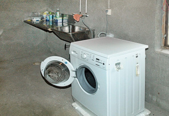 Waschmaschine mit offener Tür in einem einfachen Hauswirtschaftsraum mit Spülbecken in Schweden.