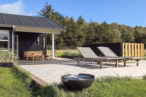 Terraza de madera con tumbonas y parrilla en casa vacacional en Øster Assels, Dinamarca, rodeada de naturaleza.