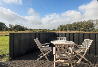 Udendørs terrasse med træbord og stole ved 6 personers feriehus i Øster Assels, Danmark, med udsigt til natur.