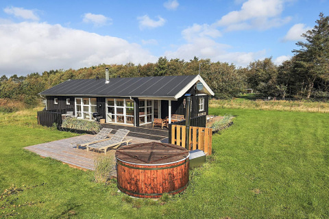 Vakantiehuis voor 6 personen in Øster Assels met houten terras, ligstoelen, hottub en grote groene tuin onder blauwe hemel.