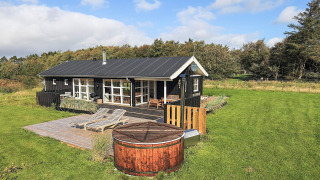 Vakantiehuis voor 6 personen in Øster Assels met houten terras, ligstoelen, hottub en grote groene tuin onder blauwe hemel.