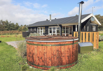 Houten hottub buiten voor een zwart vakantieverblijf met terras in Øster Assels, Denemarken.
