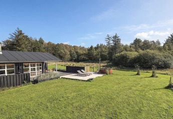 Außenaufnahme eines Ferienhauses mit Terrasse, Liegestühlen und Whirlpool im Grünen in Øster Assels, Dänemark.
