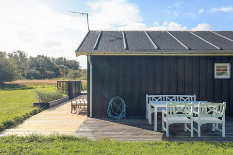 Buitenpatio met witte tuinmeubelen bij een zwart vakantiehuis in Øster Assels, Denemarken, zonnig weer.