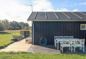 Buitenpatio met witte tuinmeubelen bij een zwart vakantiehuis in Øster Assels, Denemarken, zonnig weer.