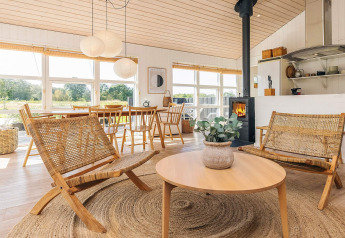 Lys og hyggelig stue i feriehus i Øster Assels, Danmark, med træmøbler og store vinduer ud til natur.