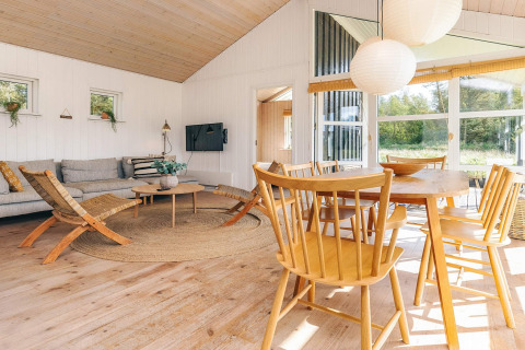 Lichte, moderne leefruimte in vakantiehuis Øster Assels, Denemarken, met houten meubels en grote ramen.