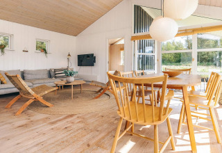 Lichte, moderne leefruimte in vakantiehuis Øster Assels, Denemarken, met houten meubels en grote ramen.