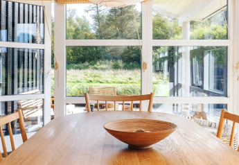 Lichte eetkamer in 6-persoons vakantiehuis in Øster Assels, Denemarken, met grote ramen en houten meubels.