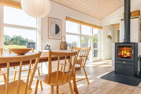 Lyst og hyggeligt sommerhus i Øster Assels med spisebord, brændeovn og store vinduer mod haven.