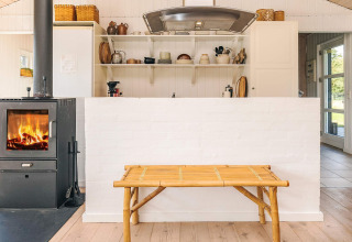 Licht interieur van een vakantiehuis in Øster Assels, Denemarken, met houtkachel en open keukenkasten.