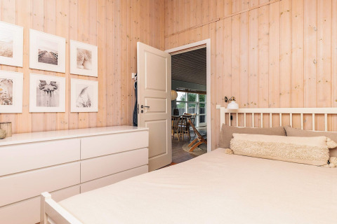Chambre avec murs en bois clair, meubles blancs et tableaux dans maison de vacances à Øster Assels, Danemark.