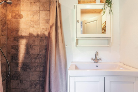 Salle de bain moderne avec lavabo, armoire miroir, douche et carrelage brun dans une maison de vacances à Øster Assels, Danemark.