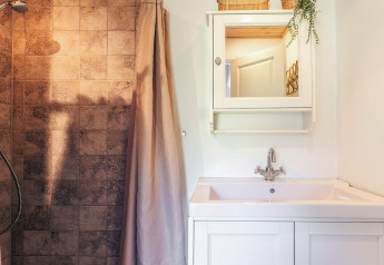 Moderne badkamer met wastafel, spiegelkast, douche en bruine tegels in een vakantiehuis in Øster Assels, Denemarken.